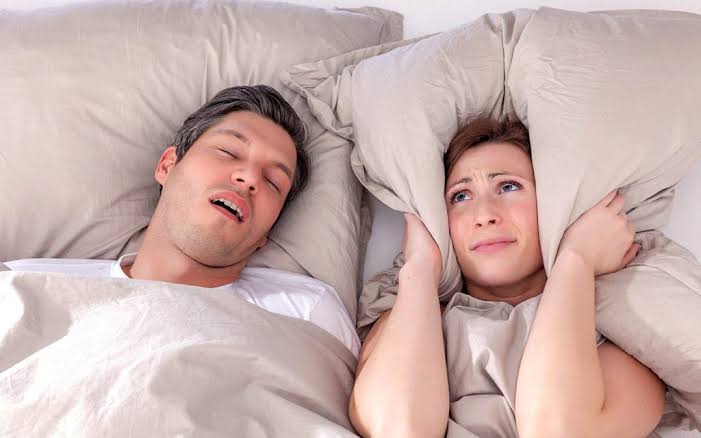 Couple in bed — one snoring while partner covers ears